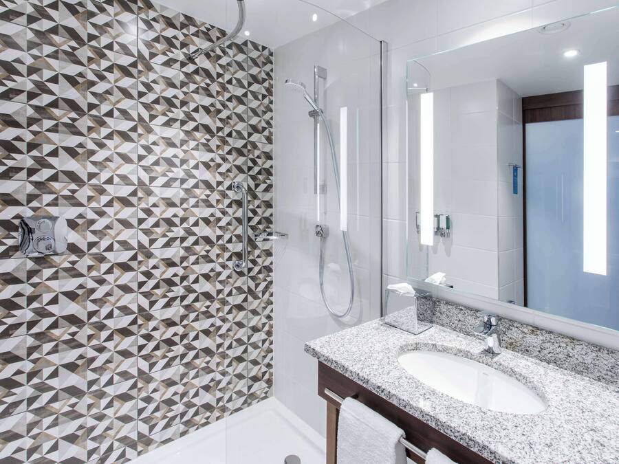 A modern bathroom with a geometric tile backsplash, a glass shower enclosure, and a granite countertop sink.