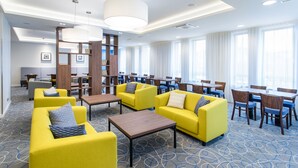 Um saguão de hotel com sofás amarelos, mesas de madeira e um grande candelabro.