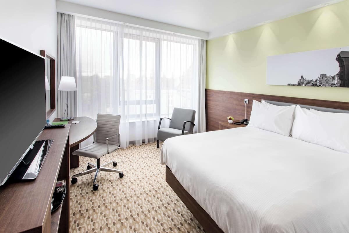 Hotelkamer met een bed, een bureau met stoel, een televisie en een raam met gordijnen.