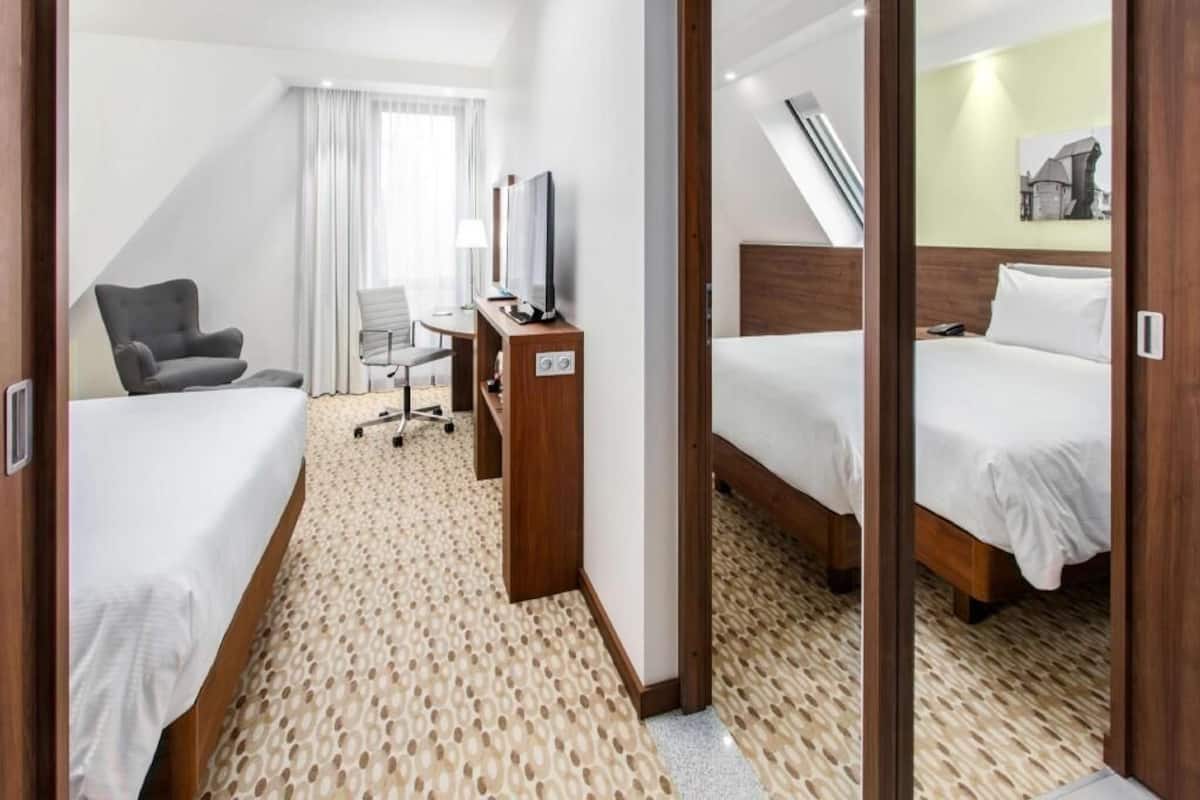 Een hotelkamer met twee bedden, een bureau met stoel, een televisie en een raam met gordijnen.