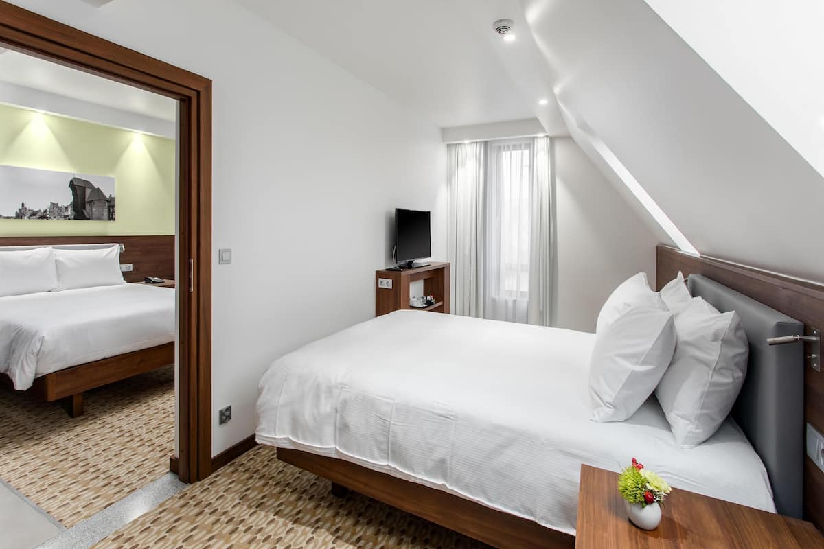 Een hotelkamer met twee bedden, een televisie, een klein tafeltje met een plant, en een stadsgezichtschilderij aan de muur.