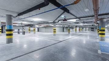 Un vaste espace de stationnement intérieur doté d’un sol en béton et de piliers marqués de bandes jaunes et noires.