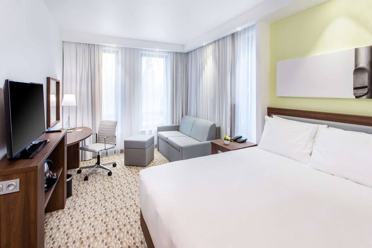 Een hotelkamer met een bed, een bureau met een televisie, een stoel, een bank en een tafeltje met een telefoon en een plant.