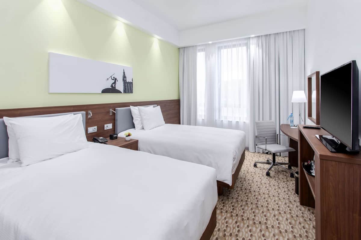 Een hotelkamer met twee bedden, een bureau met een televisie, een stoel, een lamp en een schilderij aan de muur.