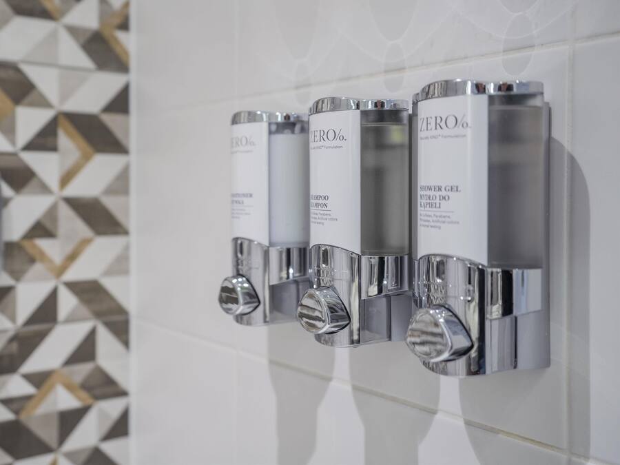 A bathroom with a geometric tile backsplash and a wall-mounted shampoo dispenser.