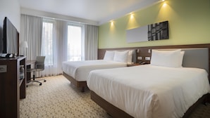 Quarto de hotel com duas camas, uma escrivaninha com cadeira, televisão e um quadro na parede.