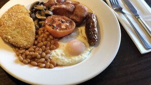 Une assiette de nourriture pour le petit-déjeuner comprenant des œufs au plat, des saucisses, des haricots et une tranche de pain grillé.