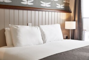 A neatly made bed with white linens and a grey throw blanket, a wooden headboard with vertical paneling, and a bedside lamp.