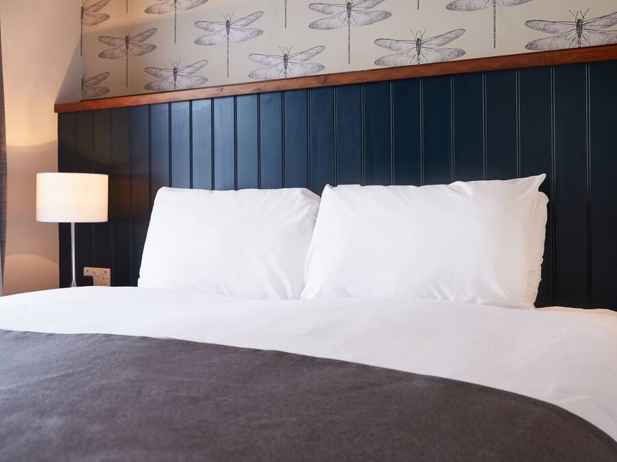 Ein Hotelzimmer mit einem Bett, weißer Bettwäsche, einem dunkelblauen Kopfteil und einer Wand mit Libellenmuster.