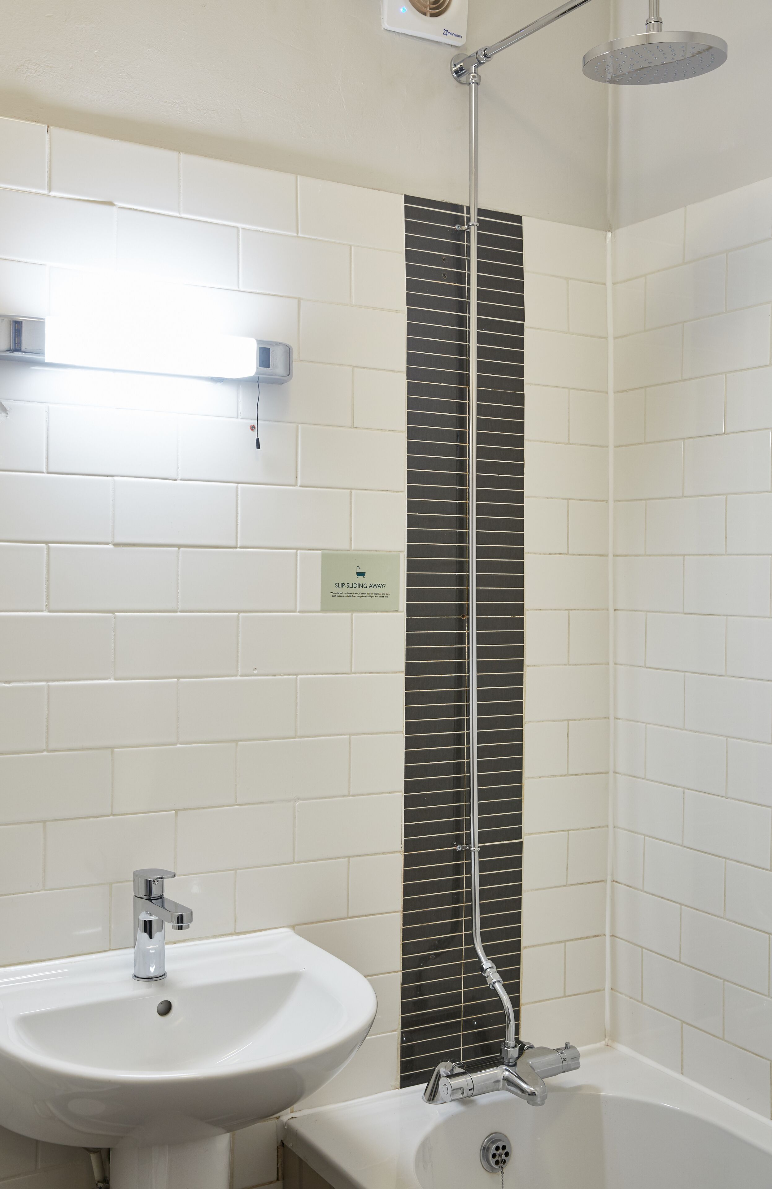 A bathroom with a white sink, a bathtub, and a shower with a black tile accent wall.