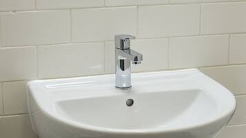 A white bathroom sink with a chrome faucet against a tiled wall.