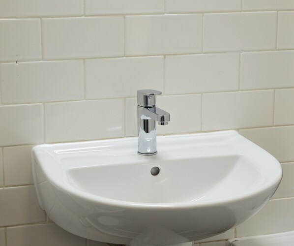 A white bathroom sink with a chrome faucet against a tiled wall.