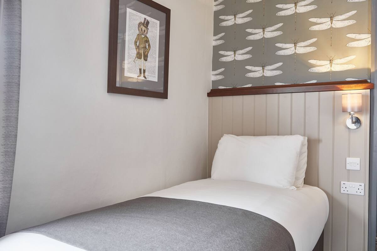 Quarto de hotel com cama, quadro emoldurado na parede e luminária fixada na parede.