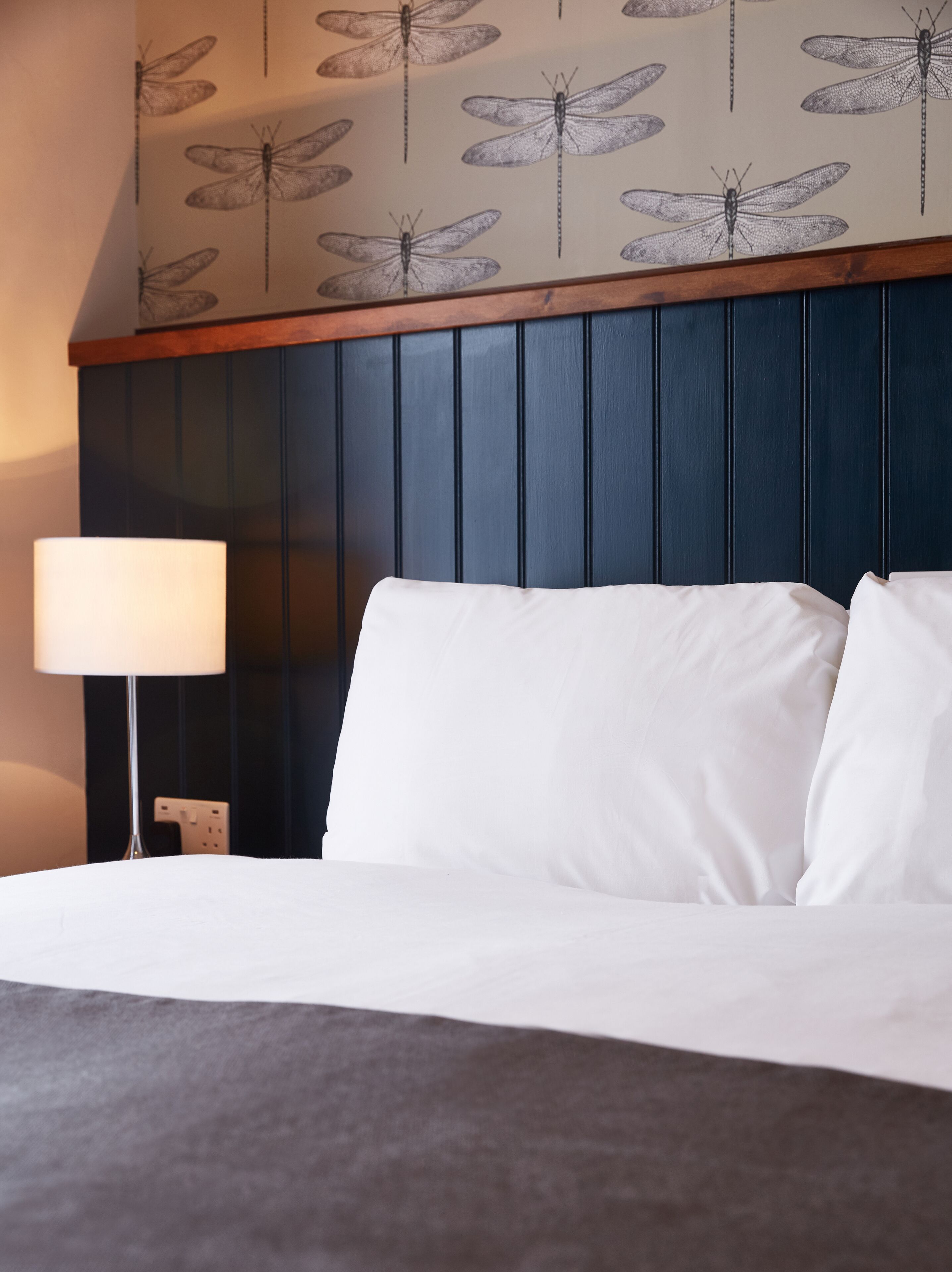 A hotel room with a bed, a nightstand, a lamp, and a wall with a dragonfly pattern.