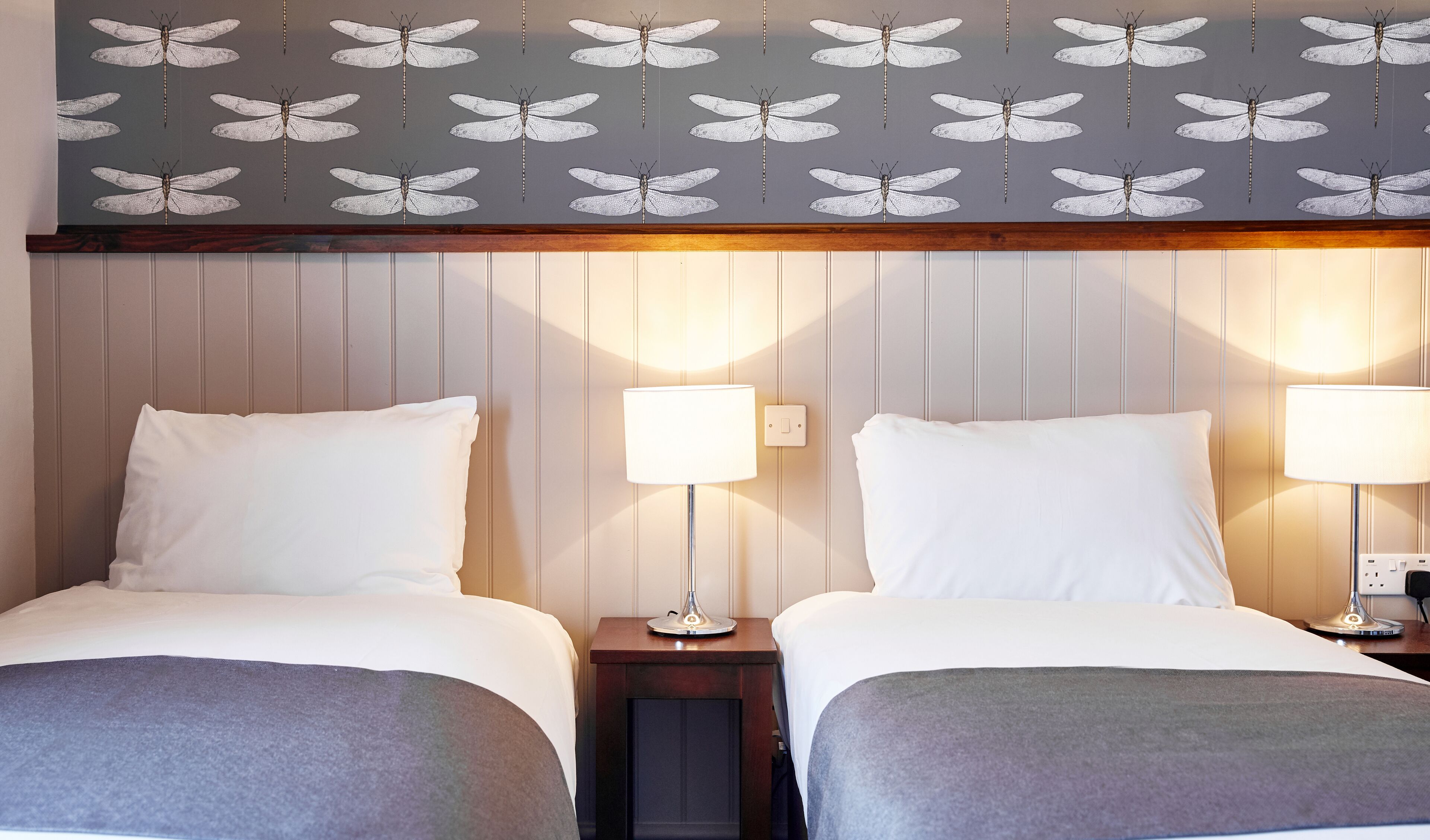 Ett hotellrum med två sängar, en vägg med ett motiv av en nyckelpiga och sänglampor.
