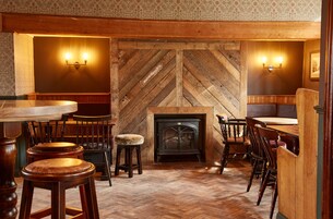 A cozy interior with wooden flooring, a fireplace, and a bar area with stools and tables.