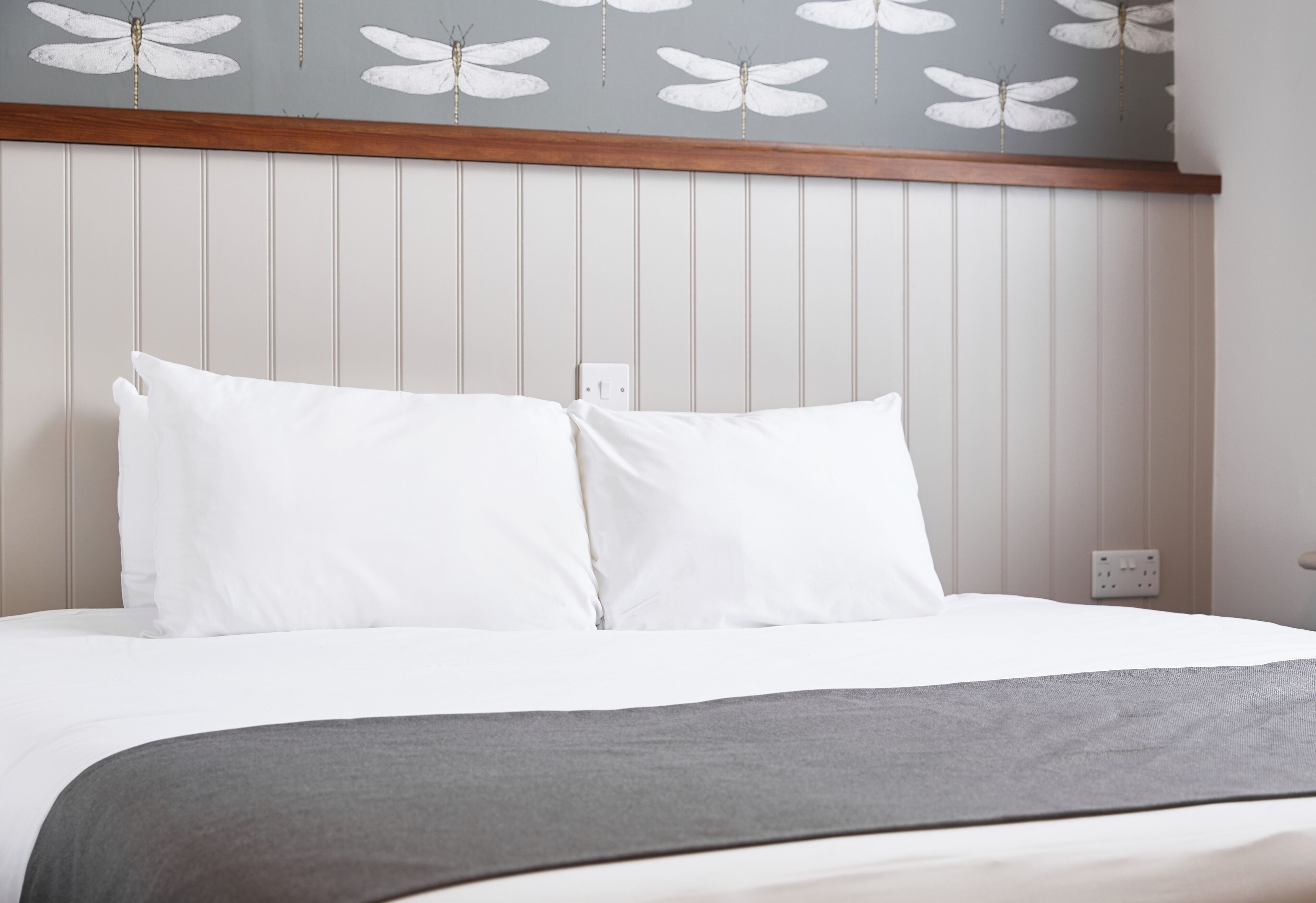 Una cama bien hecha con ropa de cama blanca y una manta gris.