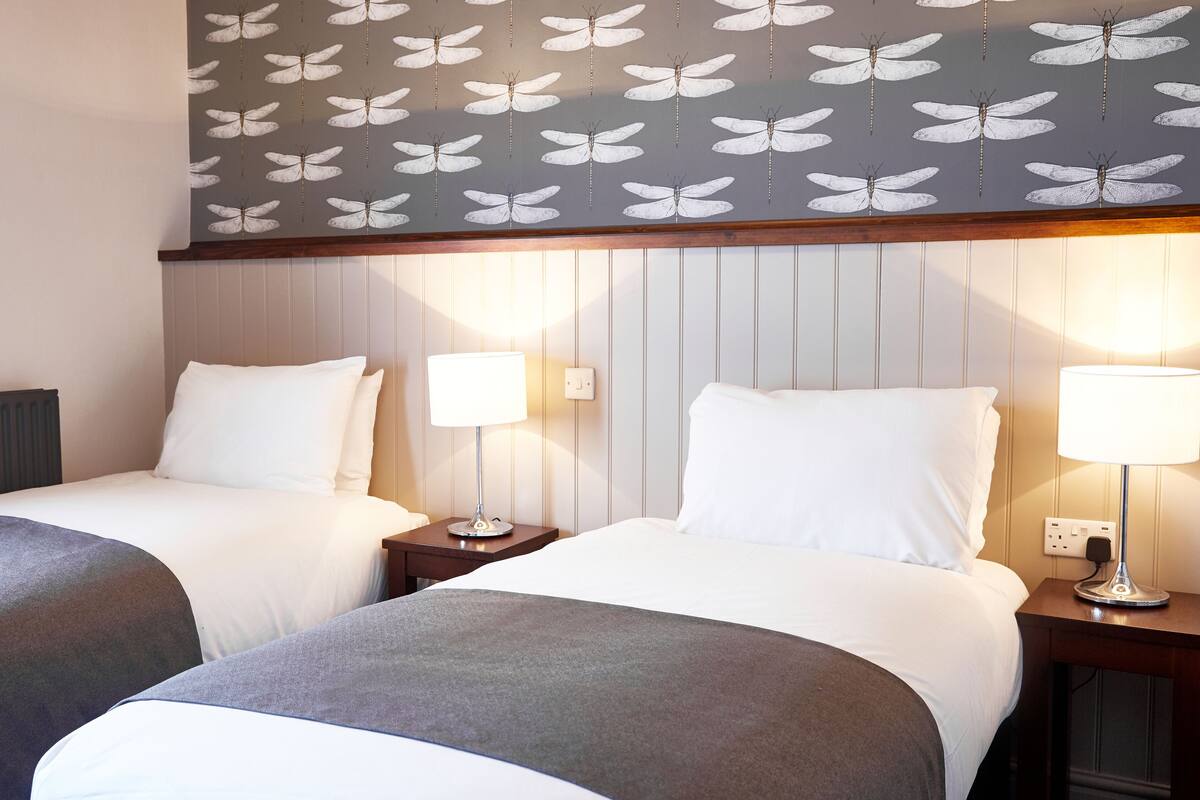 Quarto de hotel com duas camas de solteiro, cada uma com mesa de cabeceira e luminária, e teto estampado.