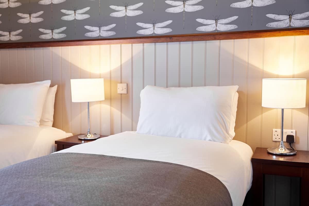 Quarto de hotel com duas camas, teto estampado e abajures de cabeceira.