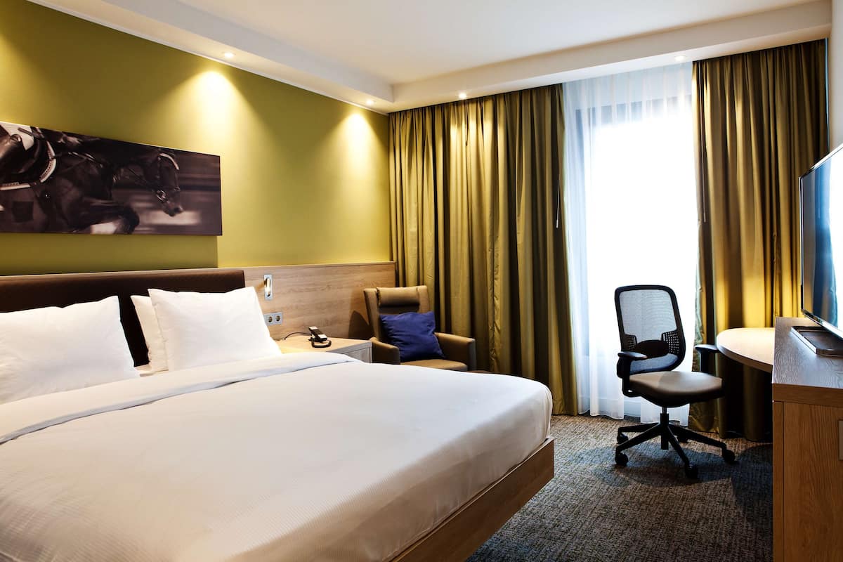 Ein Hotelzimmer mit einem großen Bett, einem Schreibtisch mit Stuhl, einem Fernseher und einem Bild an der Wand.