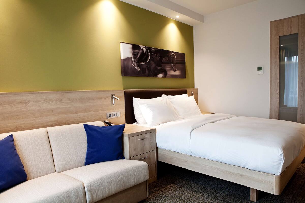 Ein Hotelzimmer mit Bett, Nachttisch, Sofa und einem an der Wand befestigten Kunstwerk.