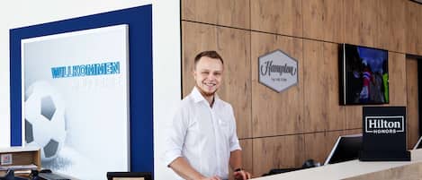 Una reception hotel con un cartello "Hilton Honors", un cartello di benvenuto e uno schermo televisivo che mostra un evento sportivo.
