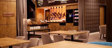 A restaurant with wooden tables and chairs, a bar area with a counter and shelves, and a sign indicating a breakfast menu.