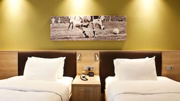 Habitación de hotel con dos camas, una mesita de noche con un reloj y un cuadro colgado en la pared de un partido de fútbol.