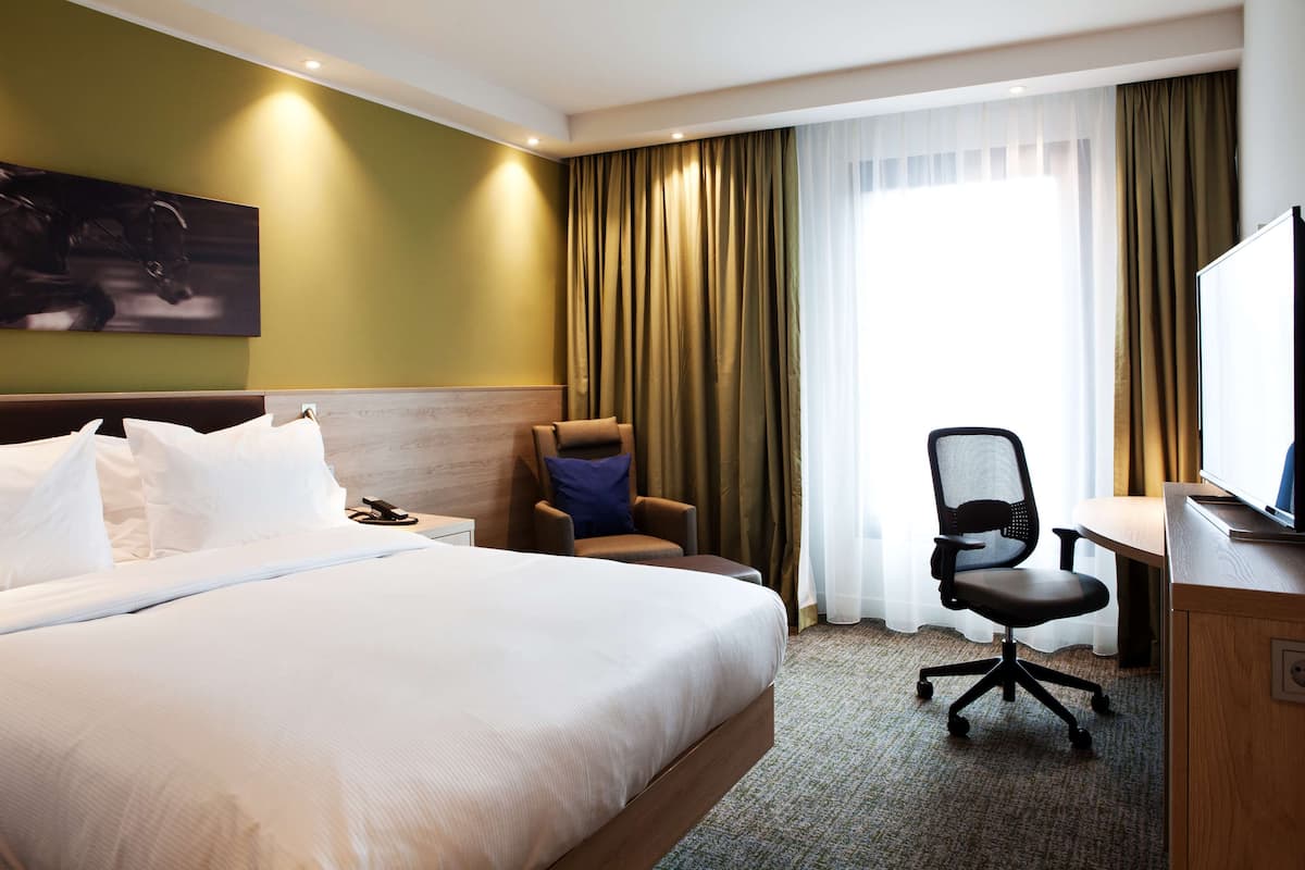 Ein Hotelzimmer mit einem großen Bett, einem Schreibtisch, einem Sessel und einem Fernseher.