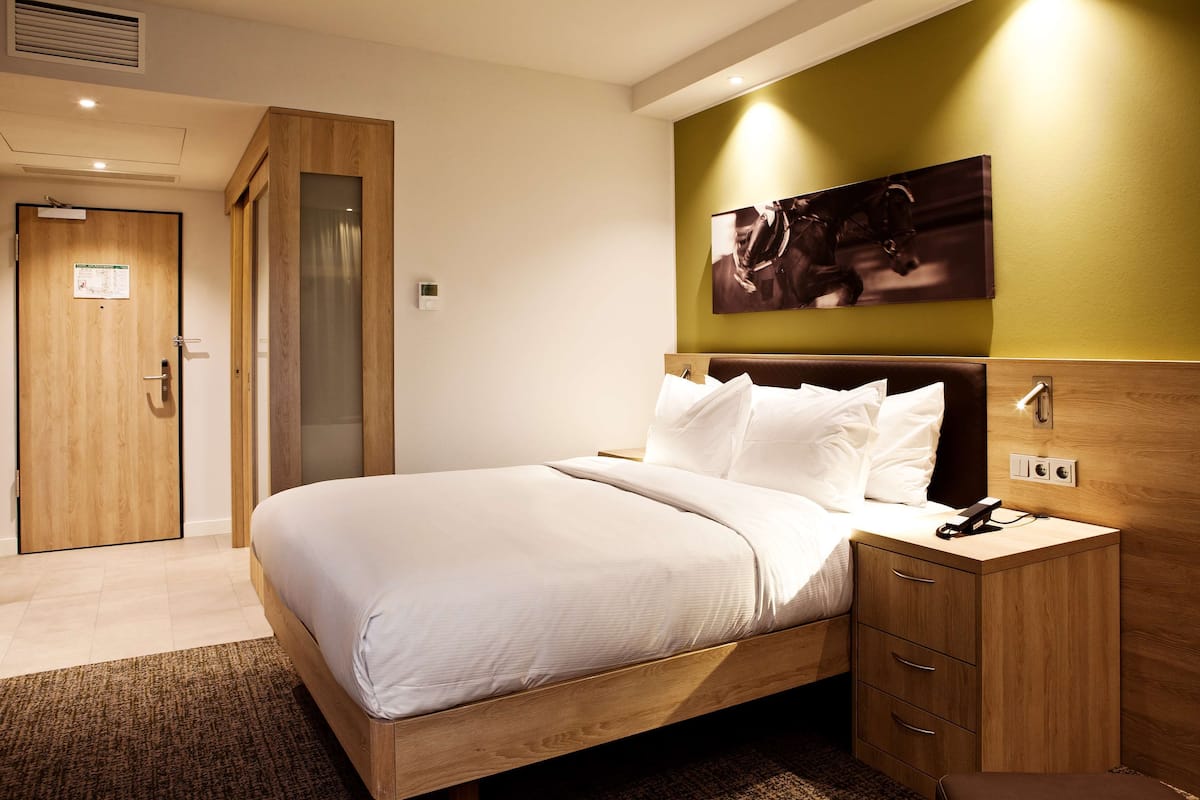 Ein modernes Hotelzimmer mit einem hölzernen Bett, einem Nachttisch und einem an der Wand befestigten Kunstwerk.