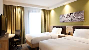 A hotel room with two beds, a desk, a chair, a TV, and a wall-mounted picture.