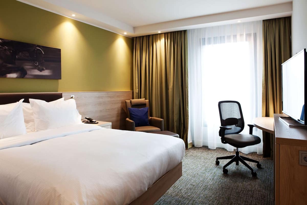 Ein Hotelzimmer mit einem großen Bett, einem Schreibtisch mit Stuhl, einem Fernseher und einem Fenster mit Vorhängen.