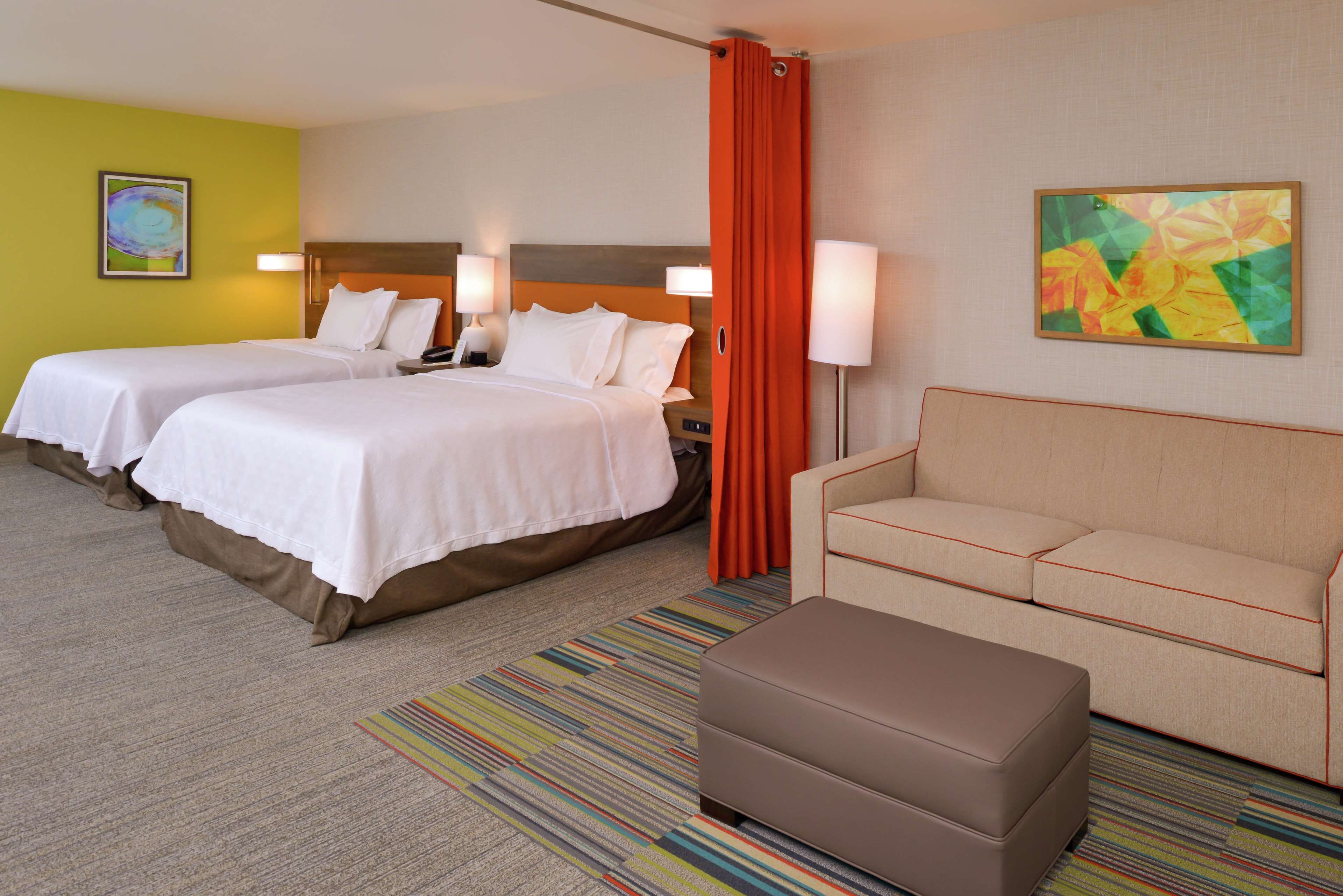 Habitación de hotel con dos camas, un sofá, una mesita y un tapete a rayas de colores.