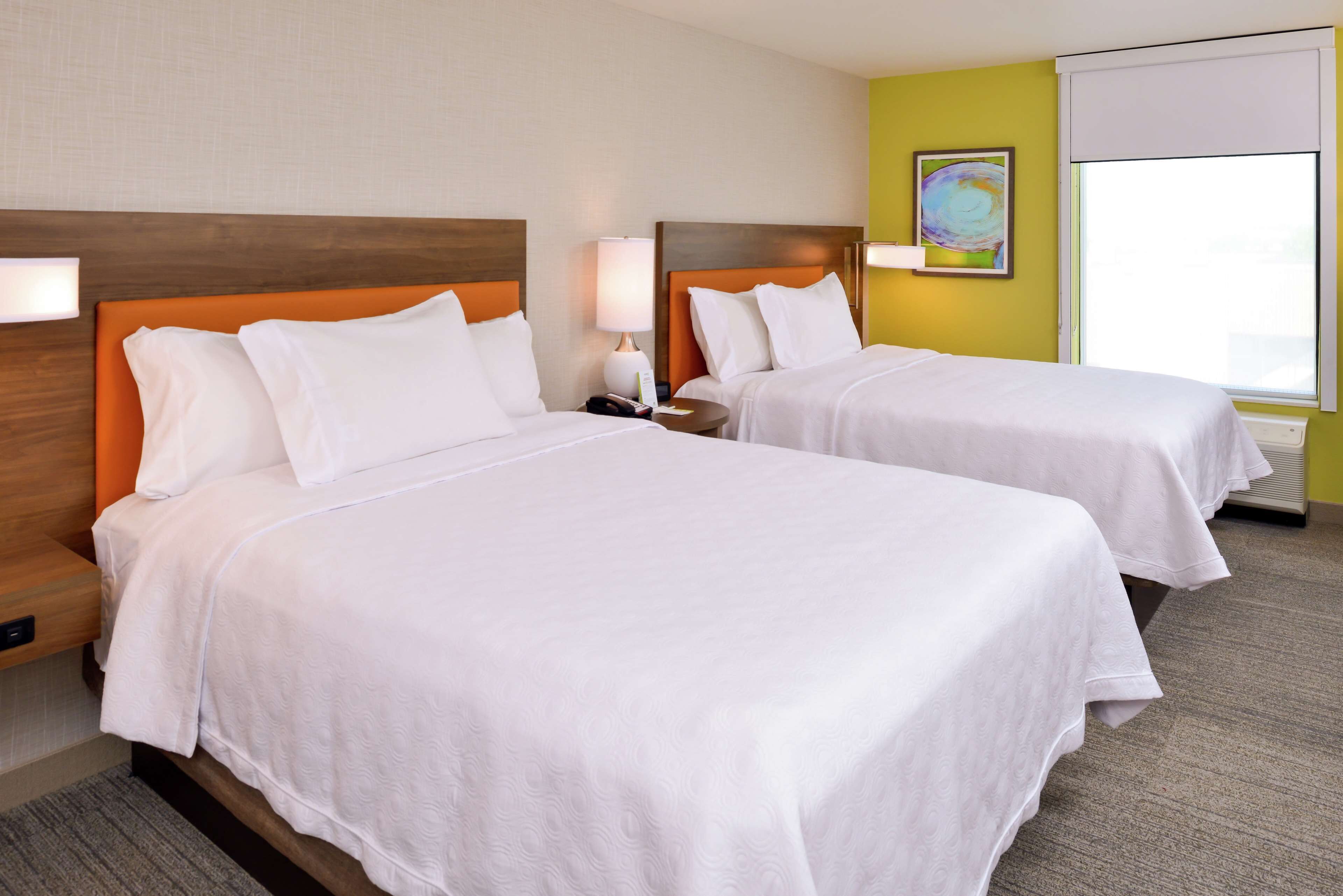 Two single beds with wooden headboards, white bedding, bedside lamps, a small table, and a window with a view.