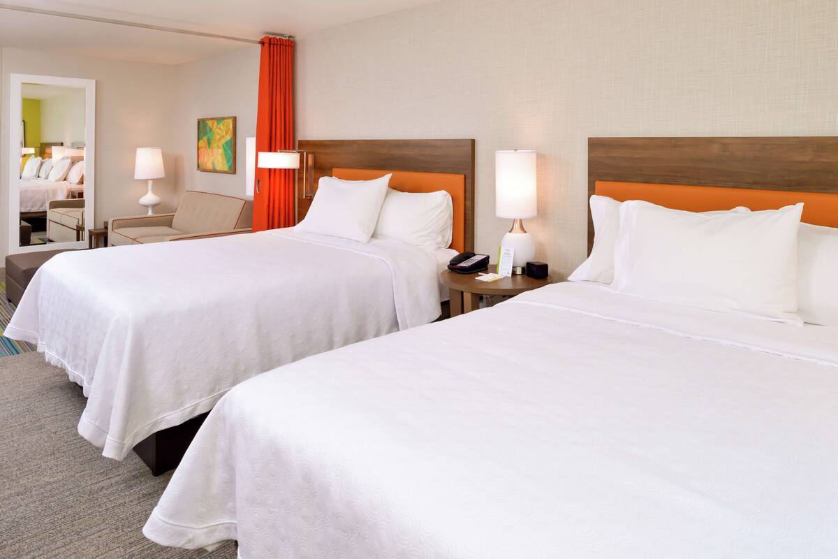Een hotelkamer met twee bedden, een zithoek met een fauteuil en een spiegel.