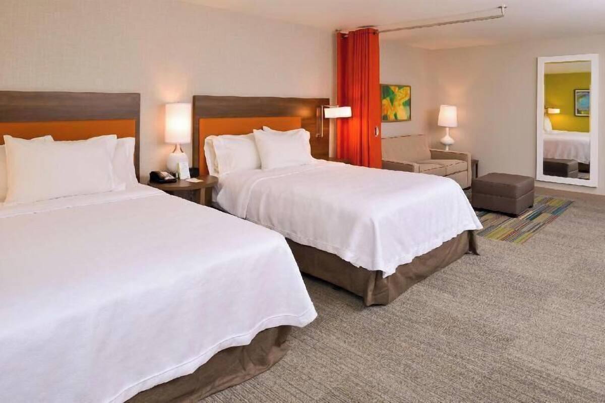 Een hotelkamer met twee bedden, een nachtkastje met lamp, een stoel, een klein tafeltje en een spiegel.