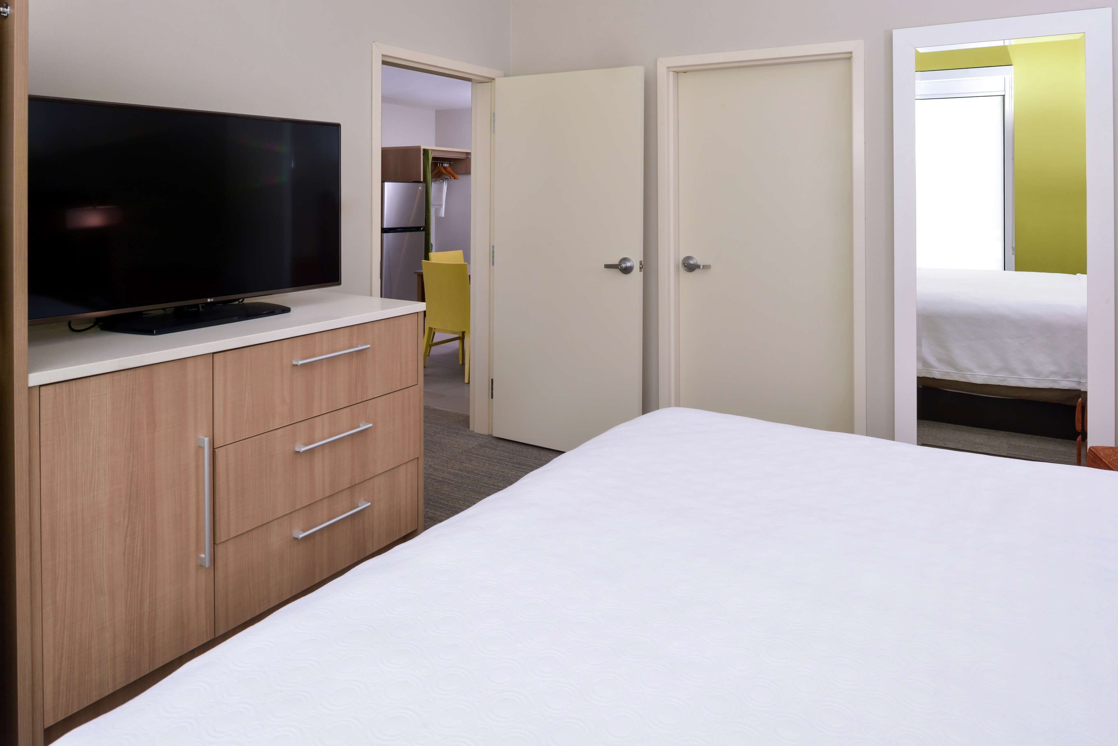 Un dormitorio con una cama, un televisor sobre un tocador de madera y un armario de dos puertas.