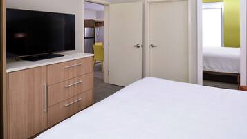 Un dormitorio con una cama, un televisor sobre un tocador de madera y un armario de dos puertas.