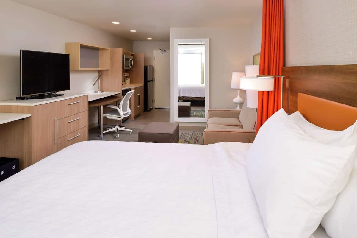 A hotel room with a bed, desk, chair, TV, and a view of the outside.