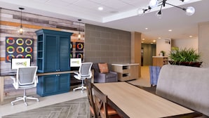 A modern interior with a wooden dining table, chairs, a sofa, and a blue cabinet. - Home2 Suites by Hilton Merrillville (Merrillville)