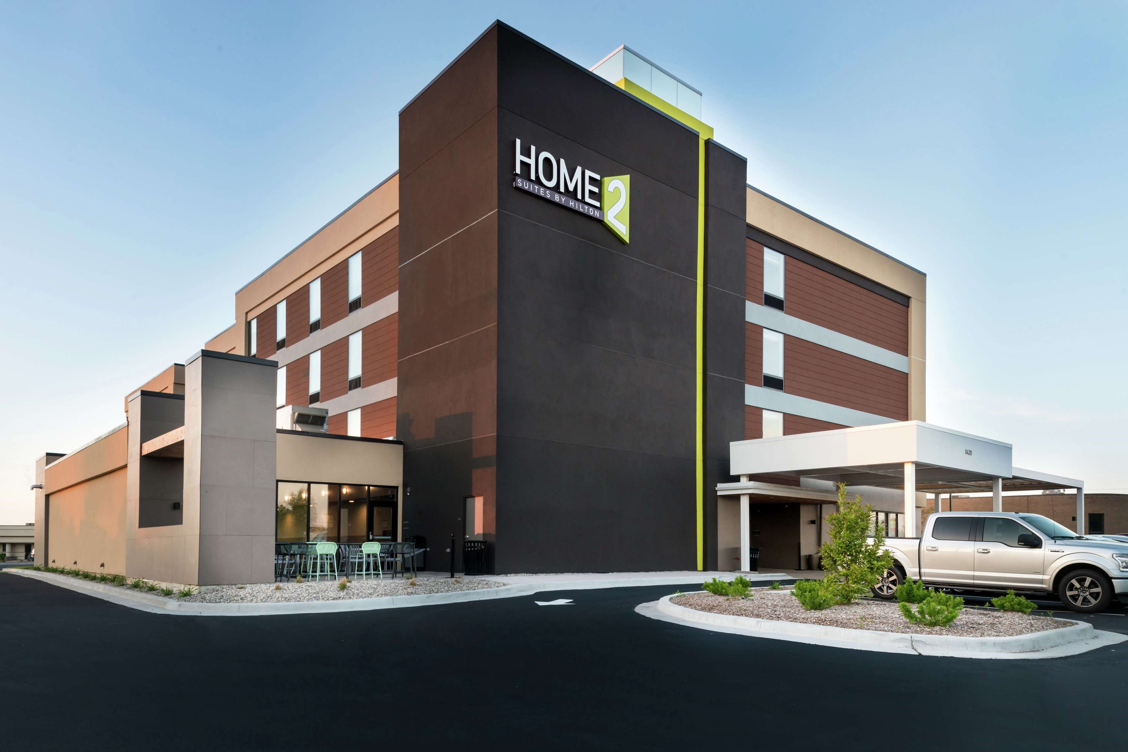 A modern hotel building with a prominent "HOME 2" sign, a covered parking area, and a landscaped entrance.