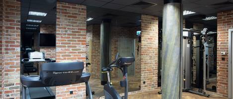 Un gimnasio con paredes de ladrillo, cinta de correr, elíptica y máquina de pesas.