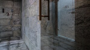 A modern bathroom with a stone wall, a glass shower enclosure, and a metal towel rack. - INX Design Hotel (Kraków)