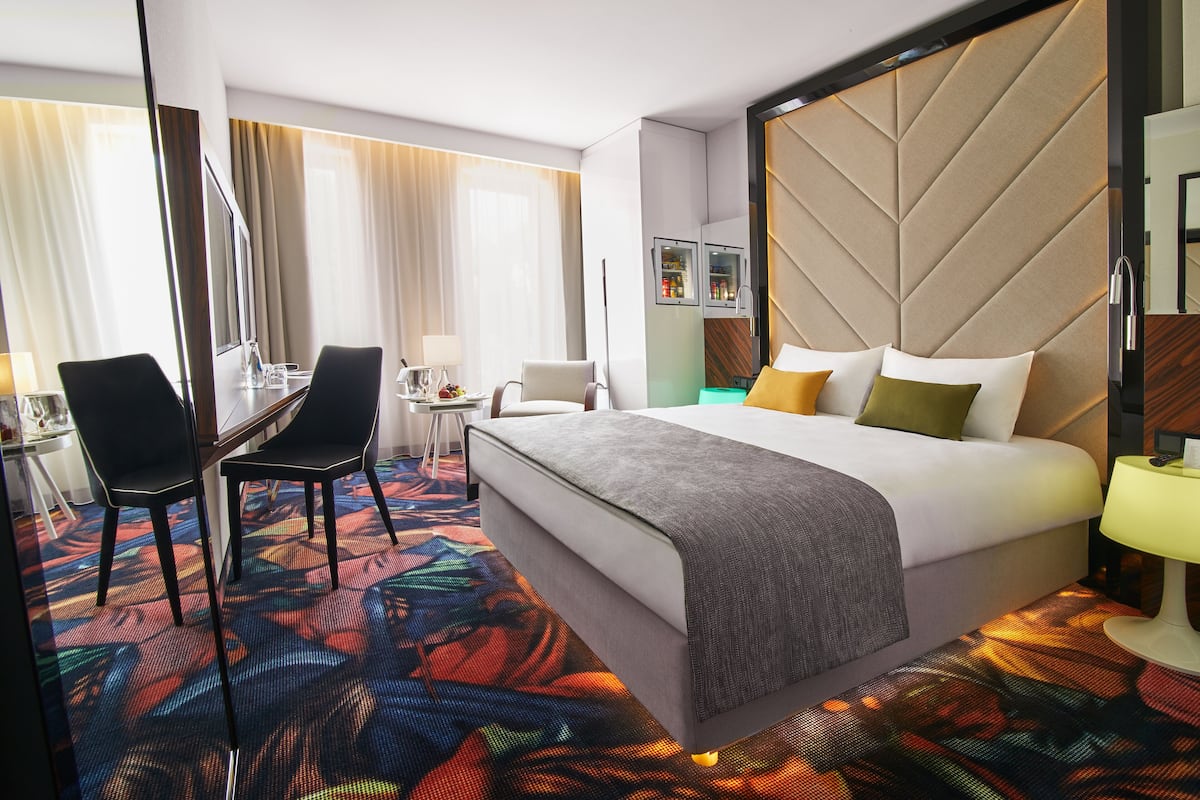 Habitación de hotel con una cama, un escritorio, dos sillas, una mesita y un televisor.