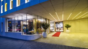 A modern hotel entrance with glass doors, a red carpet, and potted plants. - INX Design Hotel (Kraków)