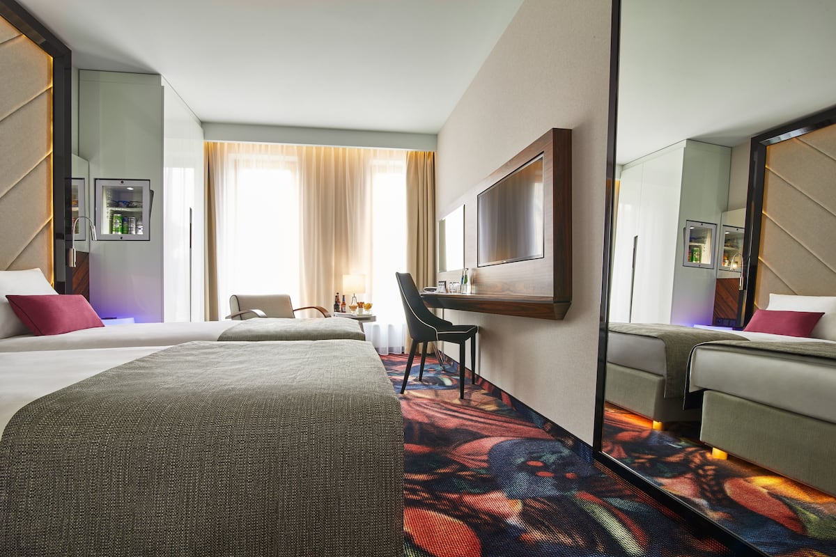 Una habitación de hotel con una cama grande, un escritorio, una silla, un espejo y una ventana con cortinas.