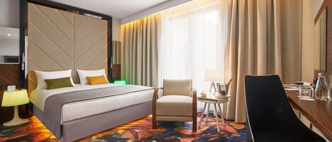 Una habitación de hotel con cama, una silla, escritorio y un ventanal con cortinas.