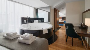 A modern hotel room with a large bathtub, a dining area with a table and chairs, and a view of the kitchen in the background. - INX Design Hotel (Kraków)