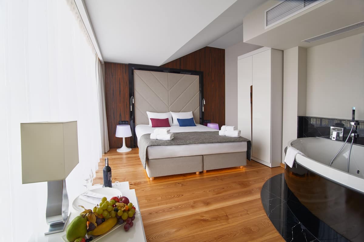 Una habitación de hotel moderna con una cama grande, un baño independiente y un área de comedor con fruta.