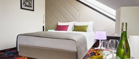A hotel room with a bed, a round table with a bottle and glasses, and a colorful carpet.